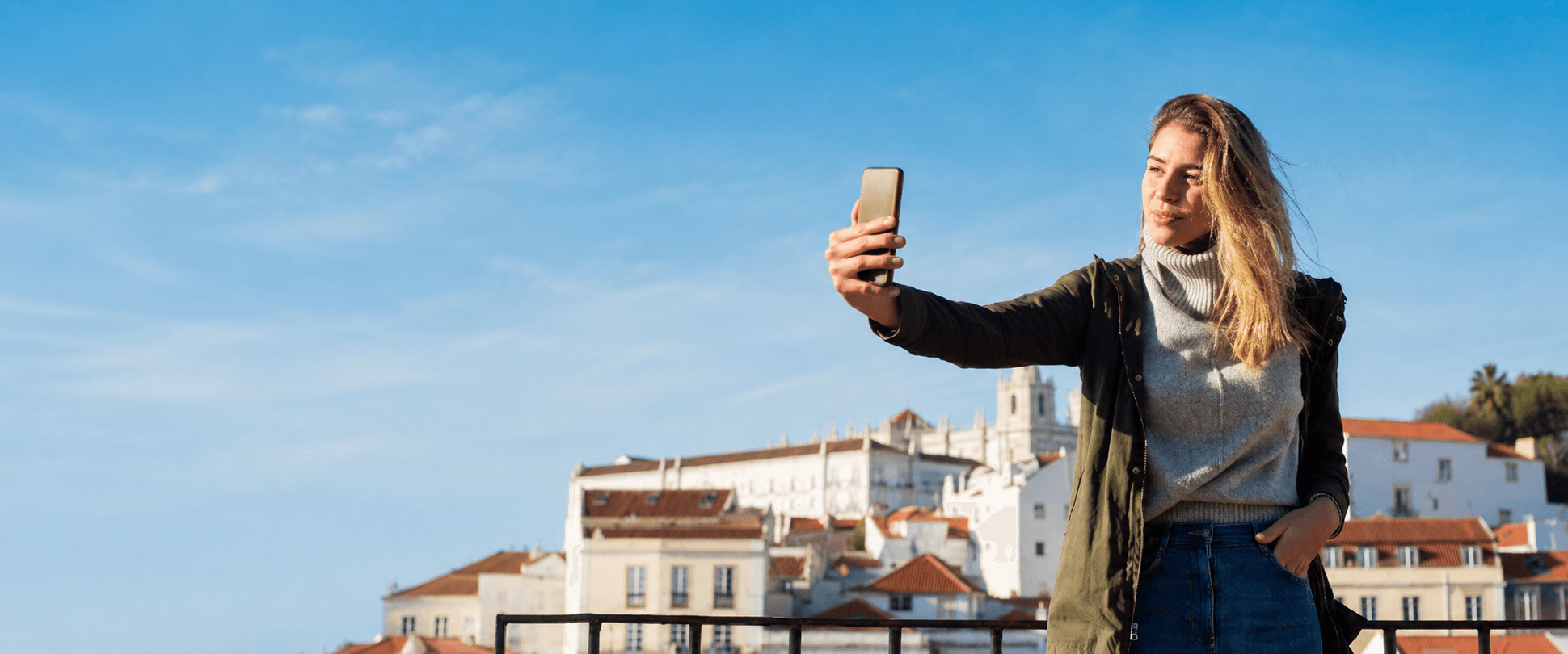 Smiling traveler holding a phone by a bright European city skyline and blue sky